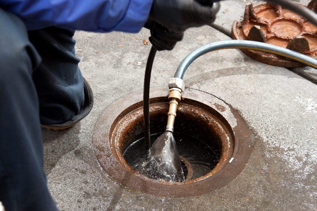 Plumber hydro jetting a sewer line through a manhole in Soledad