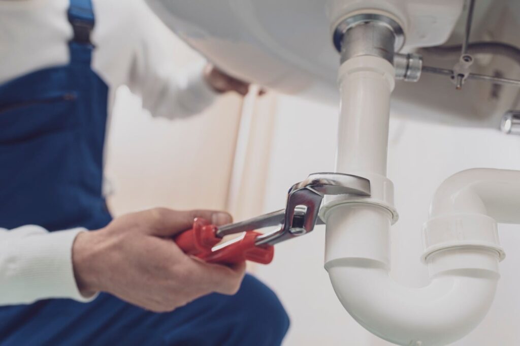 Plumber repairing a white drain pipe beneath a sink in Soledad
